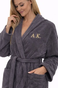 Žena v šedém froté županu střihu kimono s výšivkou monogramu AK