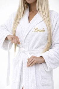 Žena v bílém županu s kapucí se zlatou výšivkou Bride