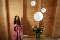 Dámský růžový bambusový župan střihu kimono - žena stojící s šálkem čaje vedle stolu s květinou